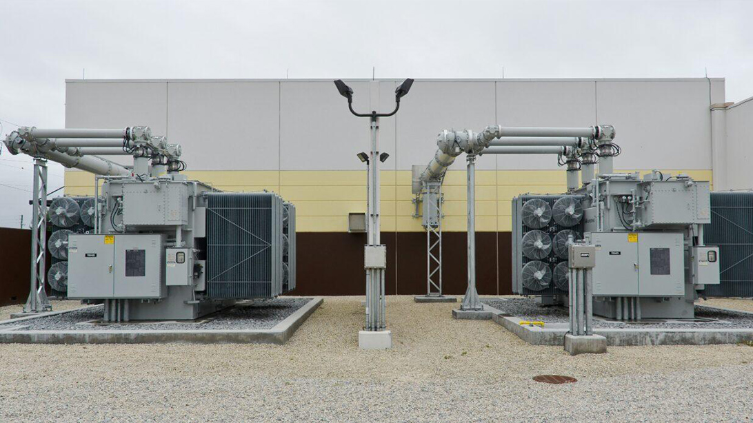 Two outdoor oil-immersed transformers with cooling fans beside an industrial building